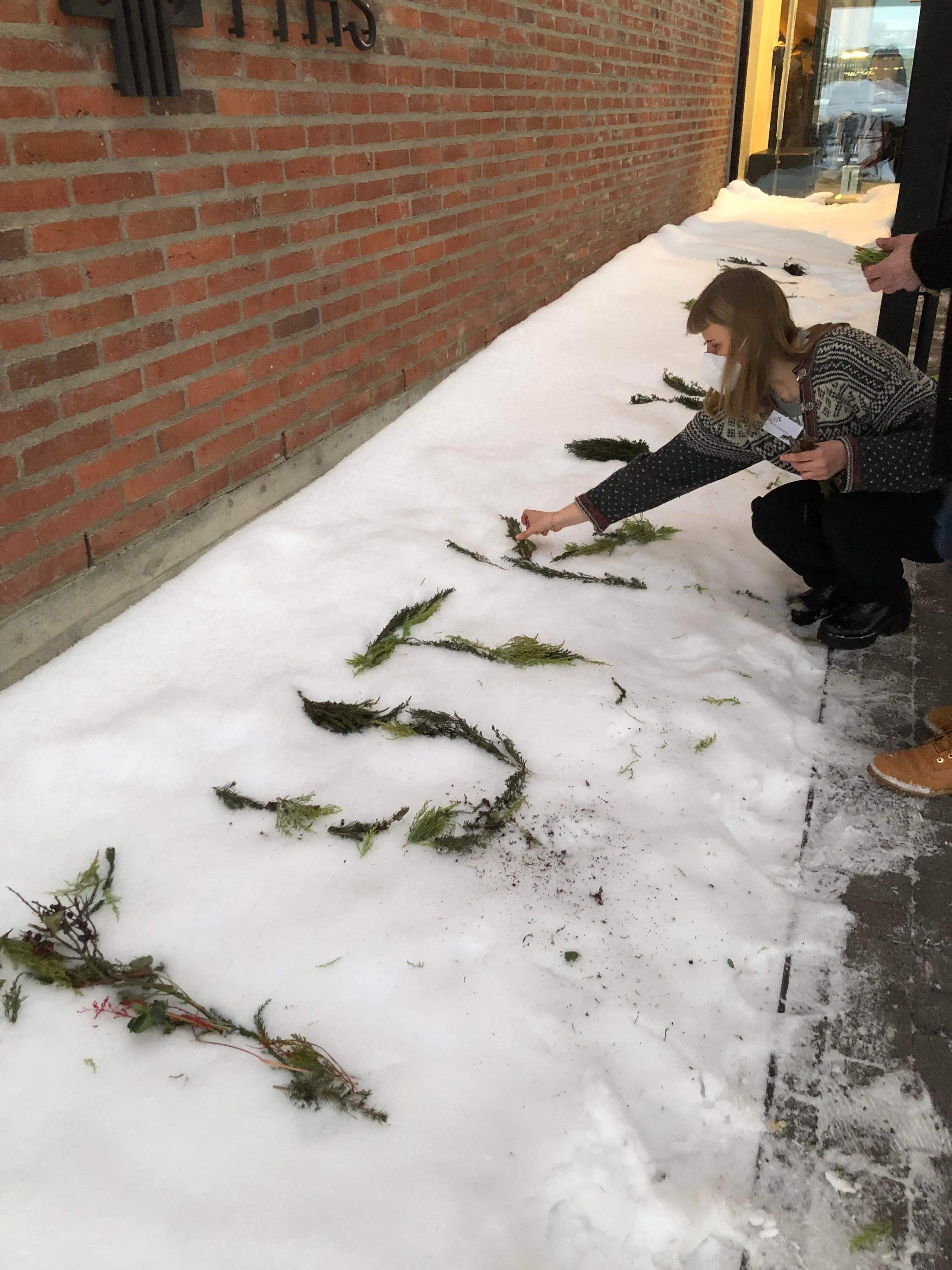 Kuvassa on rakennus, jonka eteen lumiseen maahan on muodostettu havuista ja muista kasvijätteistä sana ’tutkivismi’.
